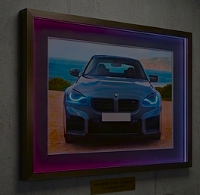 2x1.5 foot framed BMW M2 Coastal Journey car art print with built-in pink and blue LED frame lighting mounted on a modern concrete wall.