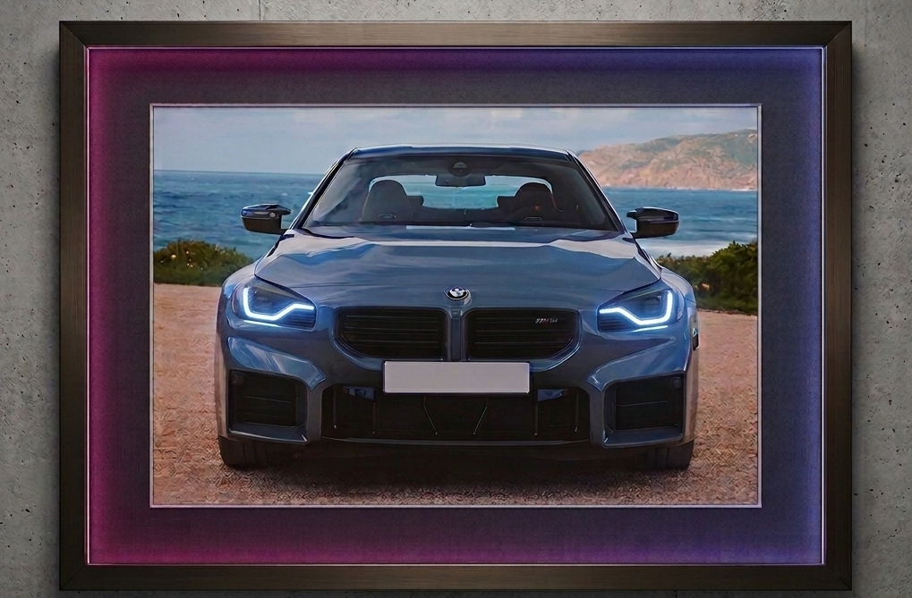 2x1.5 foot framed BMW M2 Coastal Journey car art print with built-in pink and blue LED frame lighting mounted on a modern concrete wall.