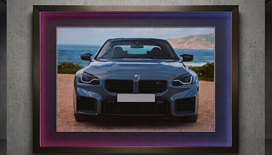 2x1.5 foot framed BMW M2 Coastal Journey car art print with built-in pink and blue LED frame lighting mounted on a modern concrete wall.